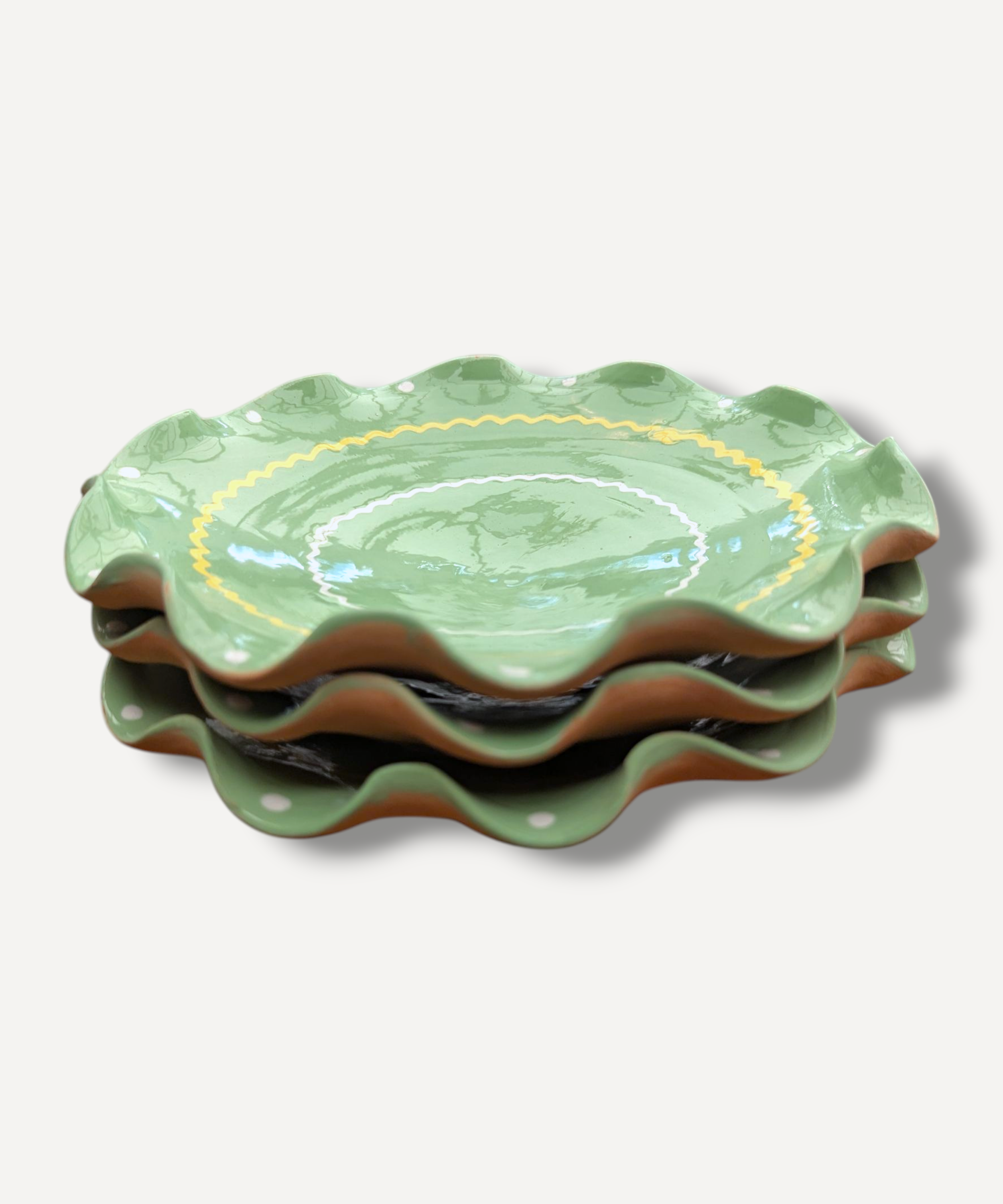 Stack of green ceramic plates with scalloped edges on a light gray background