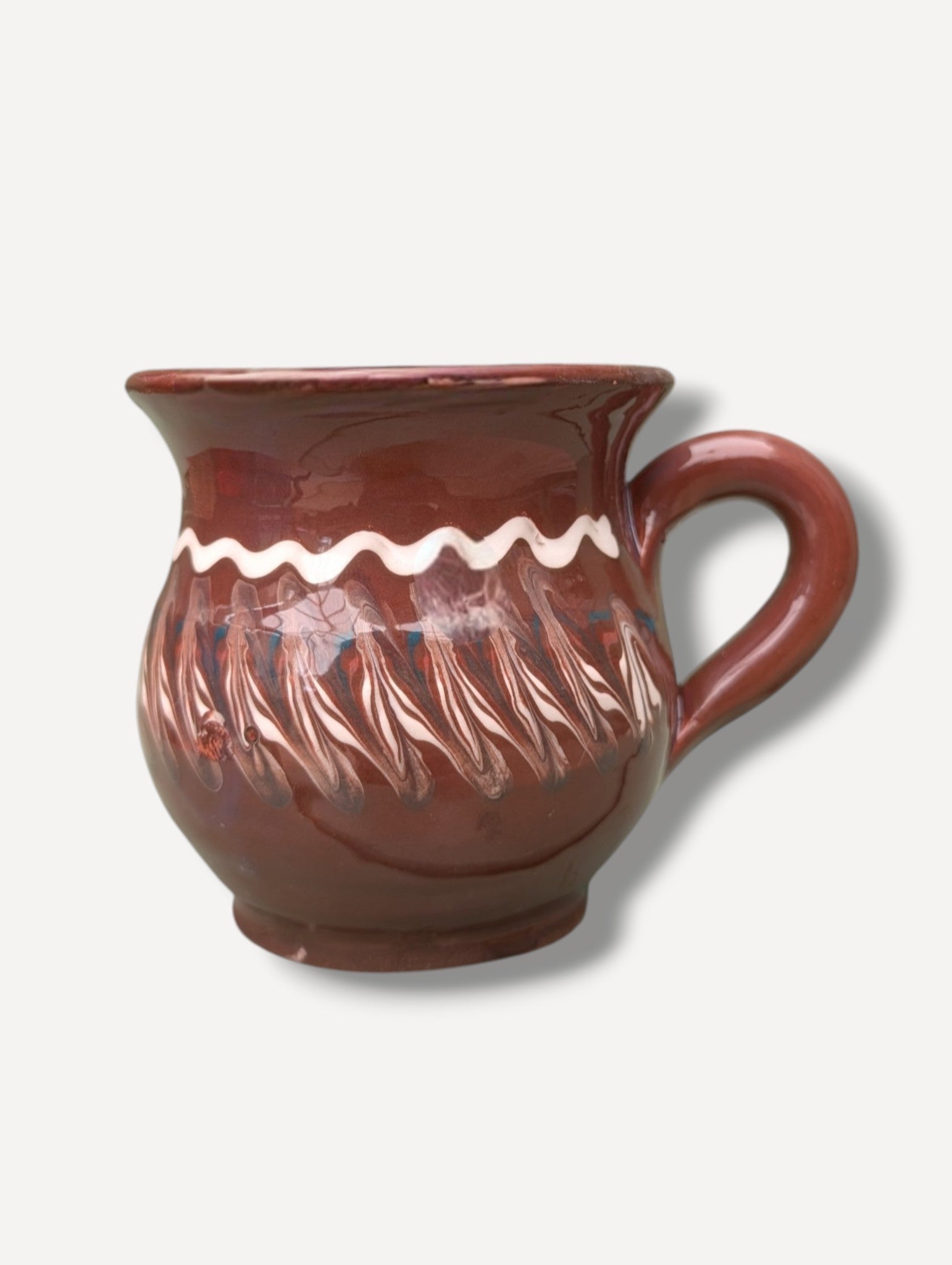 Handmade dark chocolate Romanian ceramic mug with traditional folk decoration on outdoor café table