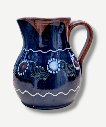 Handmade cobalt-blue Romanian earthenware jug with white floral and dotted motifs, a chocolate-brown rim and rounded body.