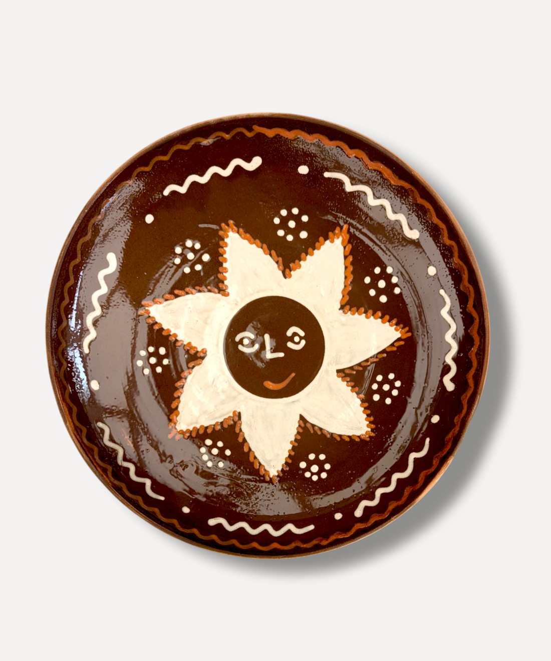 A large, handcrafted serving plate with a brown rim and a central white sun motif, decorated with traditional folk patterns.