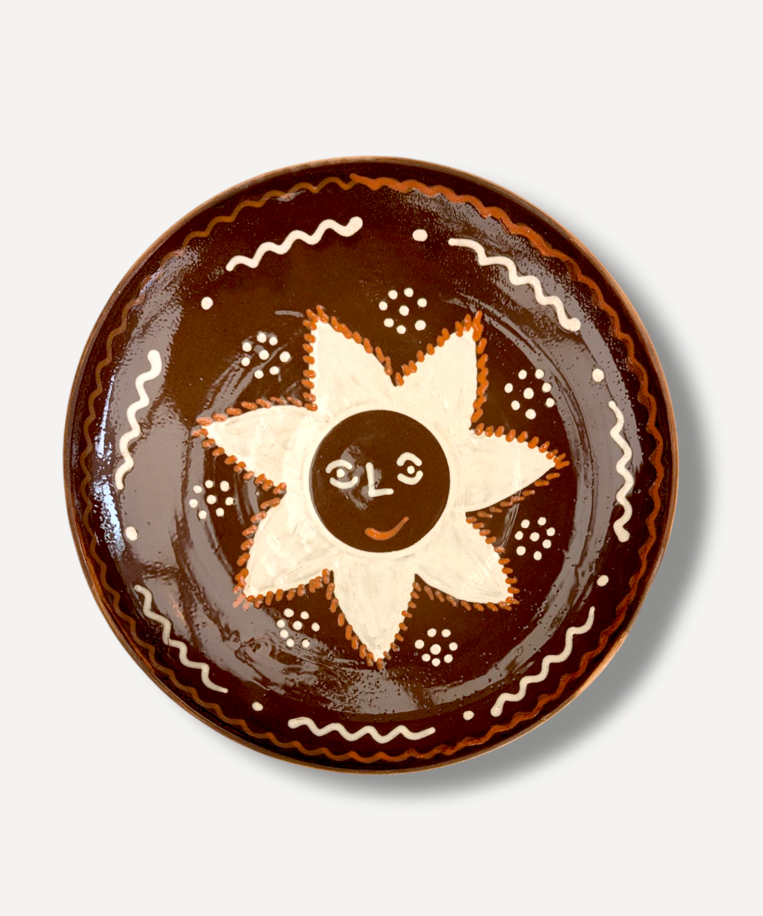 A large, handcrafted serving plate with a brown rim and a central white sun motif, decorated with traditional folk patterns.