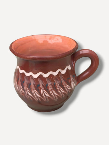 Handmade dark chocolate Romanian ceramic mug with traditional folk decoration on outdoor café table
